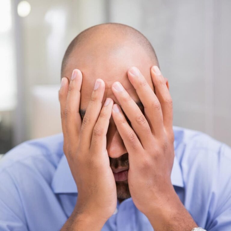 a bald man with both his hands on his face